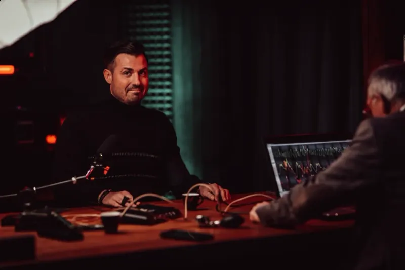 Studio: Mann im dunklen Pullover mit Messgurten am Tisch, Standbild aus dem Video